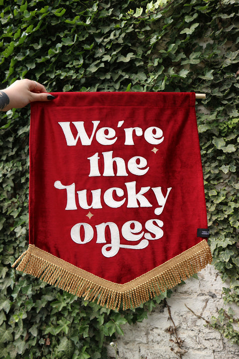 Red wedding banner saying "we're the lucky ones" on ivy backdrop.